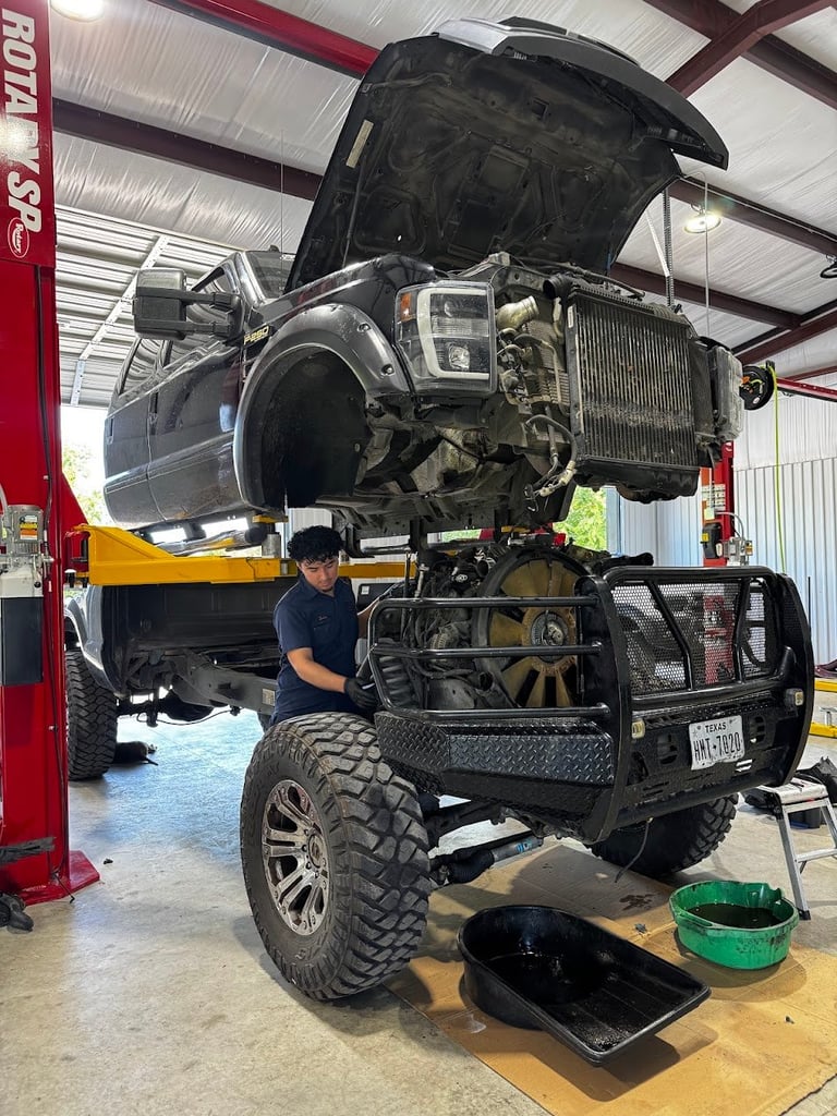 Mechanic working on lifted truck with hood open in auto shop on lift with red toolbox