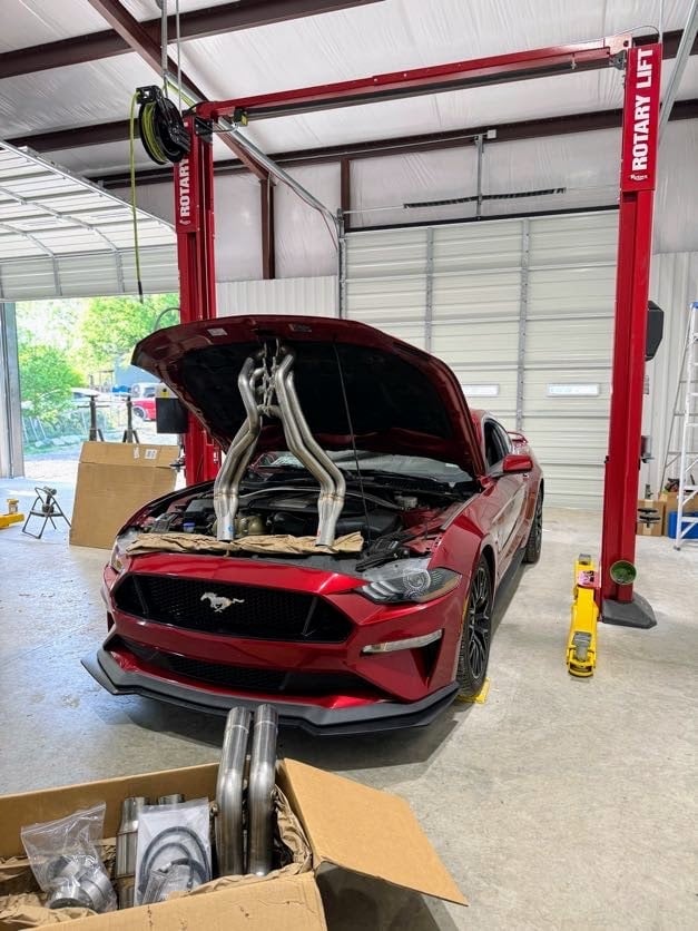 Red Ford Mustang with open hood on red lift in automotive workshop garage