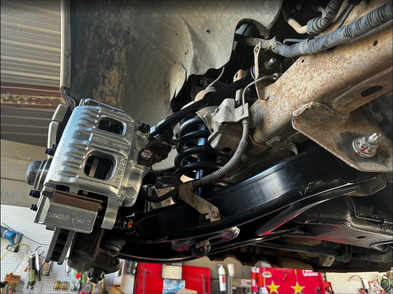 Overhead view of automotive brake system components including caliper, rotor, and mounting hardware during repair or installation