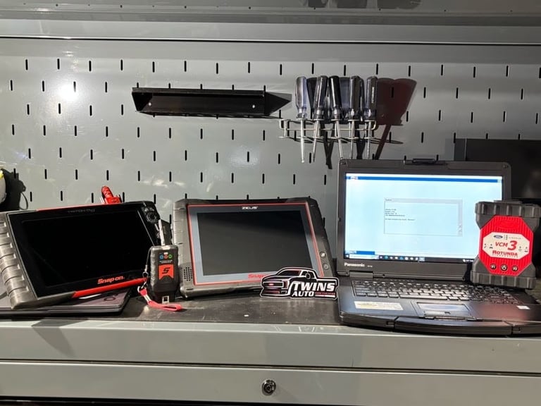 Home studio workstation with multiple monitors, laptop, microphone, and audio equipment on desk against pegboard wall